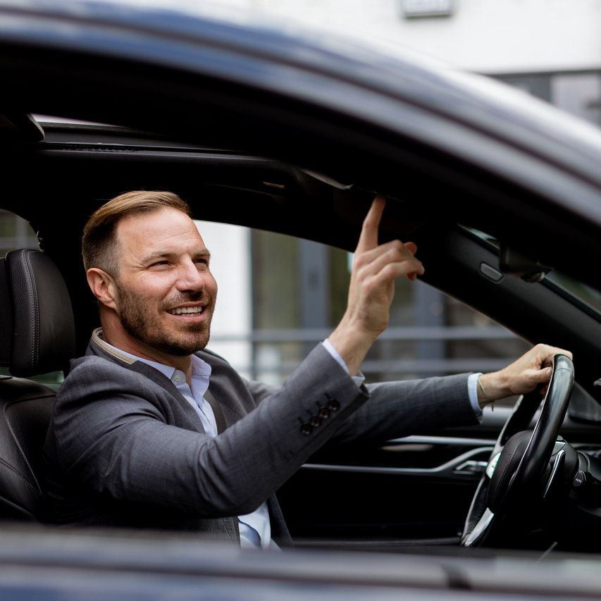 Smiling man in a suit operates his convertibles roof mechanism while parked on an urban road